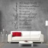Primer izgleda črne samolepilne stenske nalepke House rules 4 na sivi steni v dnevni sobi nad sedežno. Nalepka je napis, ki se glasi: In this home: We laugh loudly We make mistakes. We say I am sorry. We are patient. We cherish friends. We are grateful. We share. We love deeply.