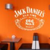 Primer izgleda bele samolepilne stenske nalepke Jack Daniels na oranžni steni v jedilnici. Nalepka je napis, ki se glasi: Jack Daniels OLD TIME Old No. 7 Brand