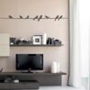 Primer izgleda črne stenska nalepka Ptički na kablu na beli steni v dnevni sobi.