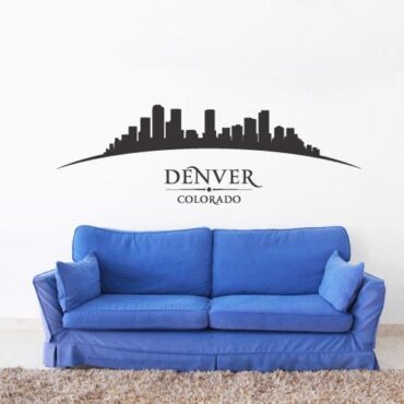 Primer izgleda črne samolepilne stenske nalepke Denver ukrivljen na beli steni nad sedežno v dnevni sobi.