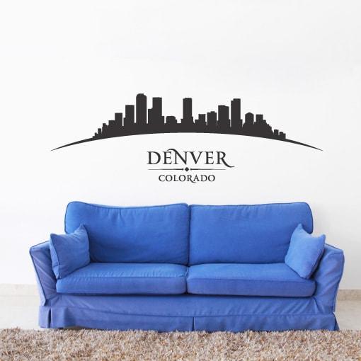 Primer izgleda črne samolepilne stenske nalepke Denver ukrivljen na beli steni nad sedežno v dnevni sobi.