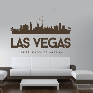 Primer izgleda čokoladno rjave samolepilne stenske nalepke Las Vegas Luna na beli steni nad zofo v dnevni sobi. Na nalepki piše: Las Vegas, United Sates of America