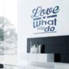 Primer izgleda črne samolepilne stenske nalepke Love what you do na beli steni v dnevni sobi. Nalepka je napis, ki se glasi: Love what you do.