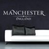 Primer izgleda bele samolepilne stenske nalepke Manchester England napis na črni steni v dnevni sobi.