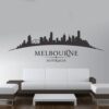Primer izgleda črne samolepilne stenske nalepke Melbourne ukrivljen na beli steni v dnevni sobi.