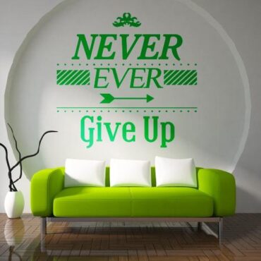 Primer izgleda zelene samolepilne stenske nalepke Never ever give up na beli steni v dnevni sobi. Nalepka je napis, ki se glasi: Never ever give up.