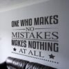 Primer izgleda črne samolepilne stenske nalepke One who makes no mistakes na beli steni v dnevni sobi. Nalepka je napis, ki se glasi: One who makes no mistakes, makes nothing at all.