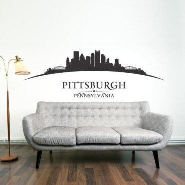 Primer izgleda črne samolepilne stenske nalepke Pittsburgh ukrivljen na beli steni v dnevni sobi. Na nalepki piše: Pittsburgh, Pennsylvania