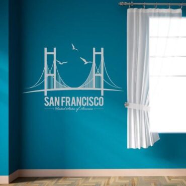 Primer izgleda bele samolepilne stenske nalepke San Francisco Brigde na modri steni v dnevni sobi. Na nalepki piše: San Francisco, United State of America