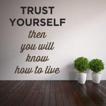 Primer izgleda dvobarvne samolepilne stenske nalepke Trust yourself then you wll know how to live na bež steni v dnevni sobi. Nalepka je napis, ki se glasi: Trust yourself and you ll know how to live.