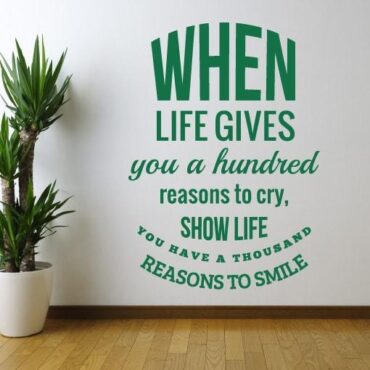 Primer izgleda zelene samolepilne stenske nalepke When life gives you a hundred reasons to cry na beli steni v dnevni sobi. Nalepka je napis, ki se glasi: When life gives you a hundred reasons to cry, Show life-You have a thousand reasons to smile.