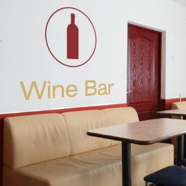 Primer izgleda dvobarvne samolepilne stenske nalepke Wine bar na beli steni v jedilnici. Nalepka je napis, ki se glasi: Wine bar.