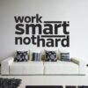 Primer izgleda črne samolepilne stenske nalepke Work smart not hard na beli steni v dnevni sobi. Nalepka je napis, ki se glasi: Work smart not hard.
