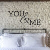 Primer izgleda črne samolepilne stenske nalepke You & me na kamniti steni v spalnici. Nalepka je napis, ki se glasi: You & me.